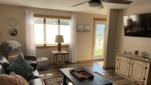 A living room with a sofa, coffee table, and a TV mounted on the wall. - Lovely Riverfront views of river. Walking distance to beach.  🚴👙🐠 (Two Rivers)