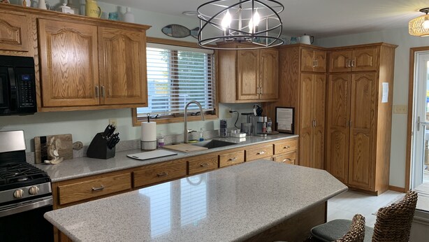 A kitchen with wooden cabinets, a granite countertop, a stainless steel stove, a sink, and a large island. - Lovely Riverfront views of river. Walking distance to beach.  🚴👙🐠 (Two Rivers)
