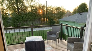 A deck with a black ottoman, wicker chairs, and a patterned rug. - Lovely Riverfront views of river. Walking distance to beach.  🚴👙🐠 (Two Rivers)