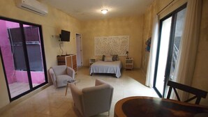 Hotelkamer met een bed, twee fauteuils, een bijzettafeltje, een decoratief wandpaneel en een groot raam met gordijnen.