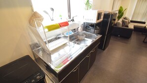 A kitchen with a built-in microwave, a sink with a dish rack, and a countertop with a kettle. - OguHouse Beppu (Beppu)