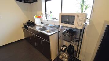 A compact kitchen with a sink, stove, microwave, and a shelf with kitchen items.