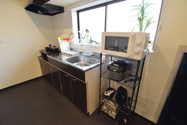 A compact kitchen with a sink, stove, microwave, and a shelf with kitchen items. - OguHouse Beppu (Beppu)