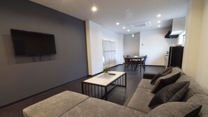 A modern living room with a flat-screen TV, a sofa, a coffee table, and a dining area in the background. - OguHouse Beppu (Beppu)