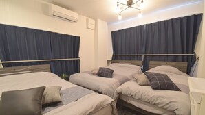 A hotel room with three beds, each with a wooden headboard, grey bedding, and dark blue curtains. - OguHouse Beppu (Beppu)