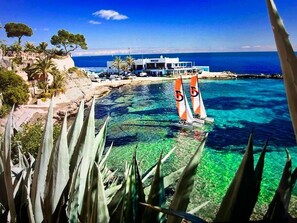 Un hotel frente al mar con aguas turquesas cristalinas, un velero y un edificio de fachada azul.