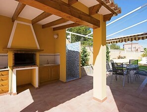 An outdoor kitchen area with a built-in grill, a stone wall, and a patio with chairs and tables. - Casa Rose Calpe 4-Bed villa with private pool (Calpe)
