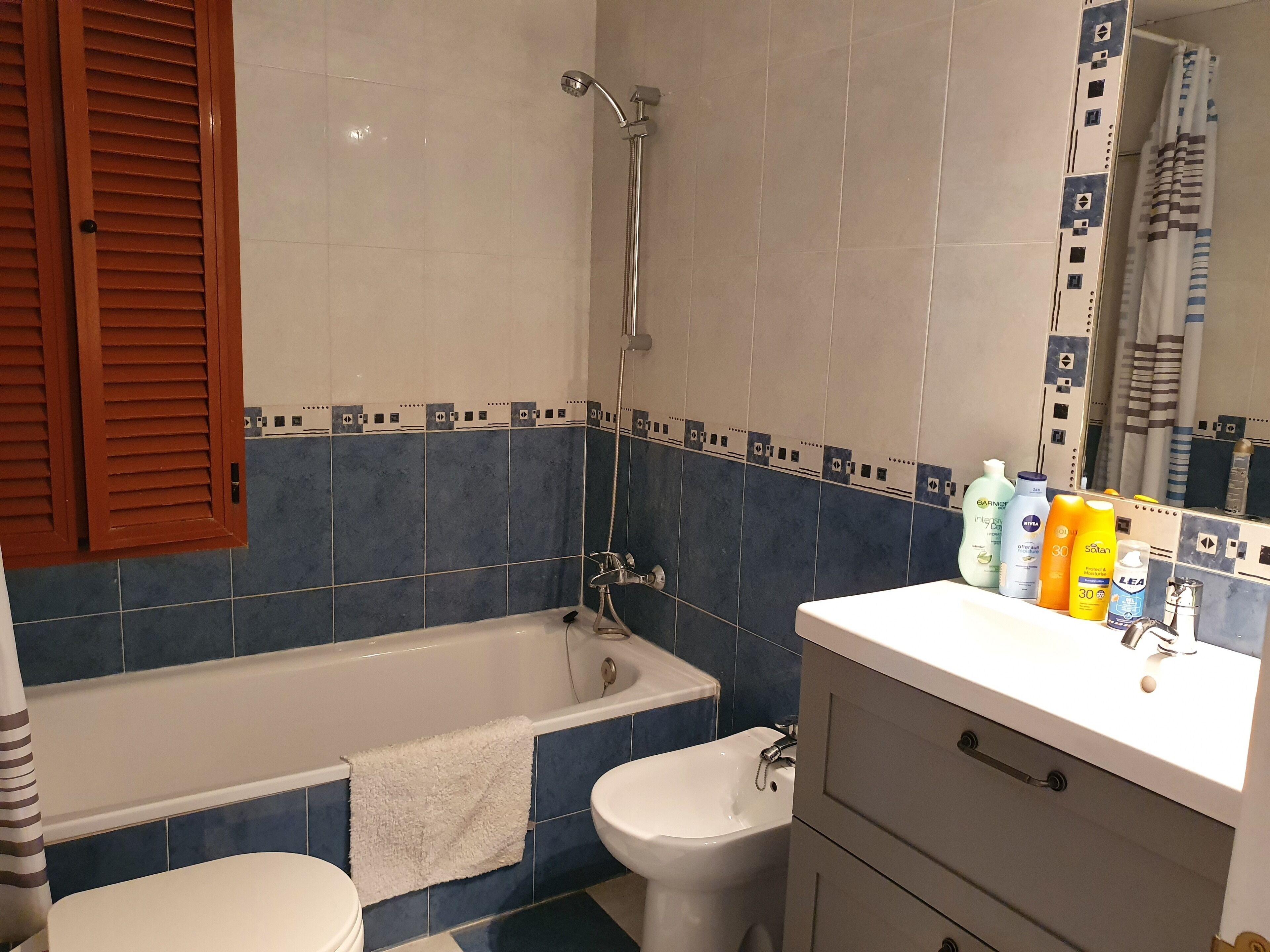 A bathroom with a bathtub, a bidet, and a toilet. There are toiletries on the counter.