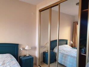 A hotel room with two beds, a wardrobe, bedside tables with lamps, and a mirror.