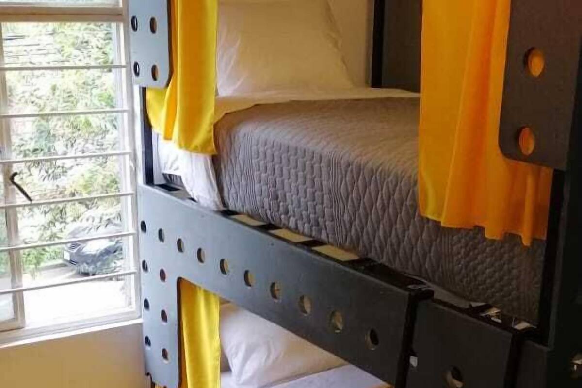 A bunk bed with yellow bedding, a window with blinds, and a wooden floor.