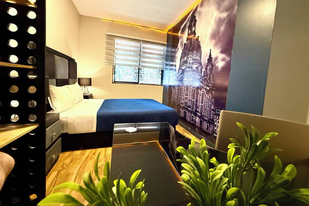 A modern bedroom with a bed, bedside table, lamp, window, and a wall with a cityscape mural.