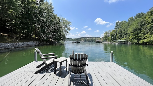 Un muelle de madera con dos sillas Adirondack y un bote de basura.