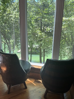 Una habitación con dos sillas negras orientadas a un ventanal con vistas a un parque verde y árboles.