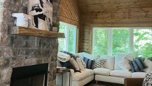 Una sala de estar acogedora con chimenea de piedra, techo de madera y un ventanal con vistas al verdor.