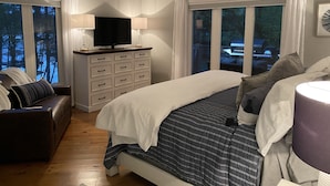 Un dormitorio con una cama, un televisor sobre un aparador, una silla y una ventana con cortinas.