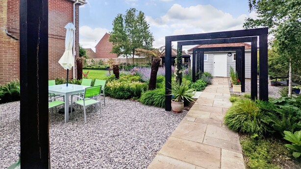 Eine Terrasse mit Tisch und Stühlen, umgeben von einem Kiesweg und verschiedenen Pflanzen.