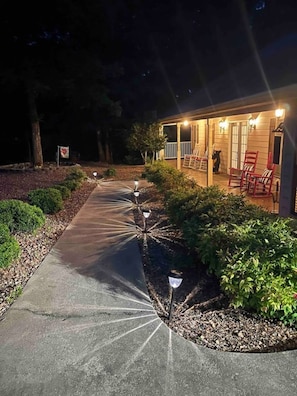 A pathway leading to a building with a porch, outdoor seating, and a well-lit entrance.