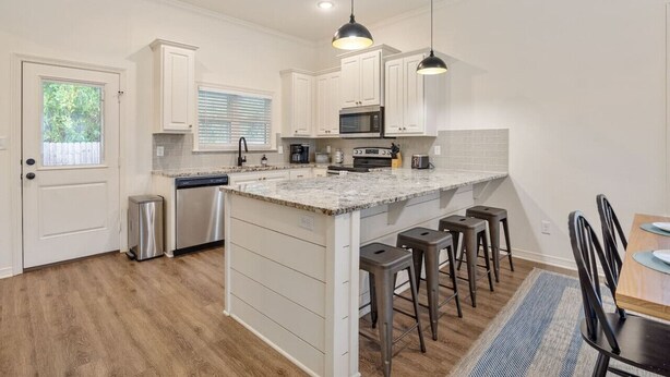 A modern kitchen with white cabinetry, a granite countertop, and a central island with bar stools.