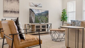 A modern living room with leather sofas, a wooden coffee table, and a large flat-screen TV mounted on the wall.