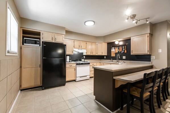 A modern kitchen with a black refrigerator, white stove, and wooden cabinets.