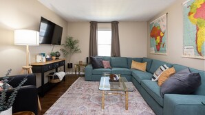 A living room with a sectional sofa, a coffee table, a TV, and a map on the wall. - Skyline - Military/Family Friendly (Shiloh)