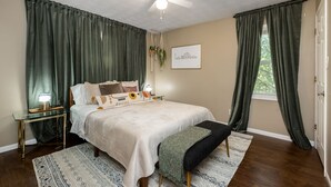 A bedroom with a bed, bedside tables, a ceiling fan, a cityscape artwork, and green curtains. - Skyline - Military/Family Friendly (Shiloh)