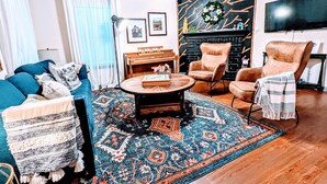 Ein Wohnzimmer mit einem blauen Sofa, einem runden Couchtisch, einem Kamin und einem Fernseher.