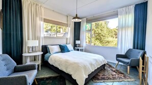 A modern bedroom with a large bed, two bedside tables, a chair, and a view of the outdoors.