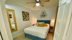 A bedroom with a bed, a ceiling fan, a wall-mounted light, and a mirror. - HEATED POOL, HOTTUBS, OCEAN/ GULF VIEW! Top Floor, Kitchen, Modern Decor! (Galveston)