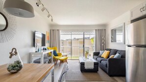 A modern living room with a sofa, coffee table, and dining area. There is a large window with a view of the outside. - HEATED POOL, HOTTUBS, OCEAN/ GULF VIEW! Top Floor, Kitchen, Modern Decor! (Galveston)