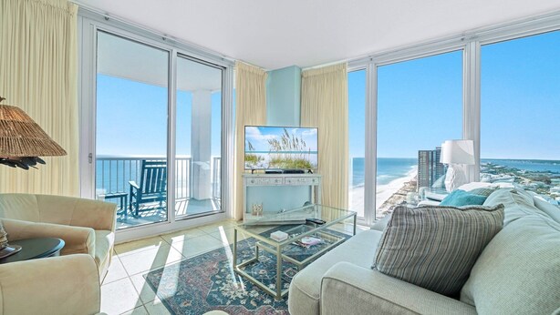 Un salón amplio con televisor grande, asientos cómodos y un balcón con vista a la playa y al océano.
