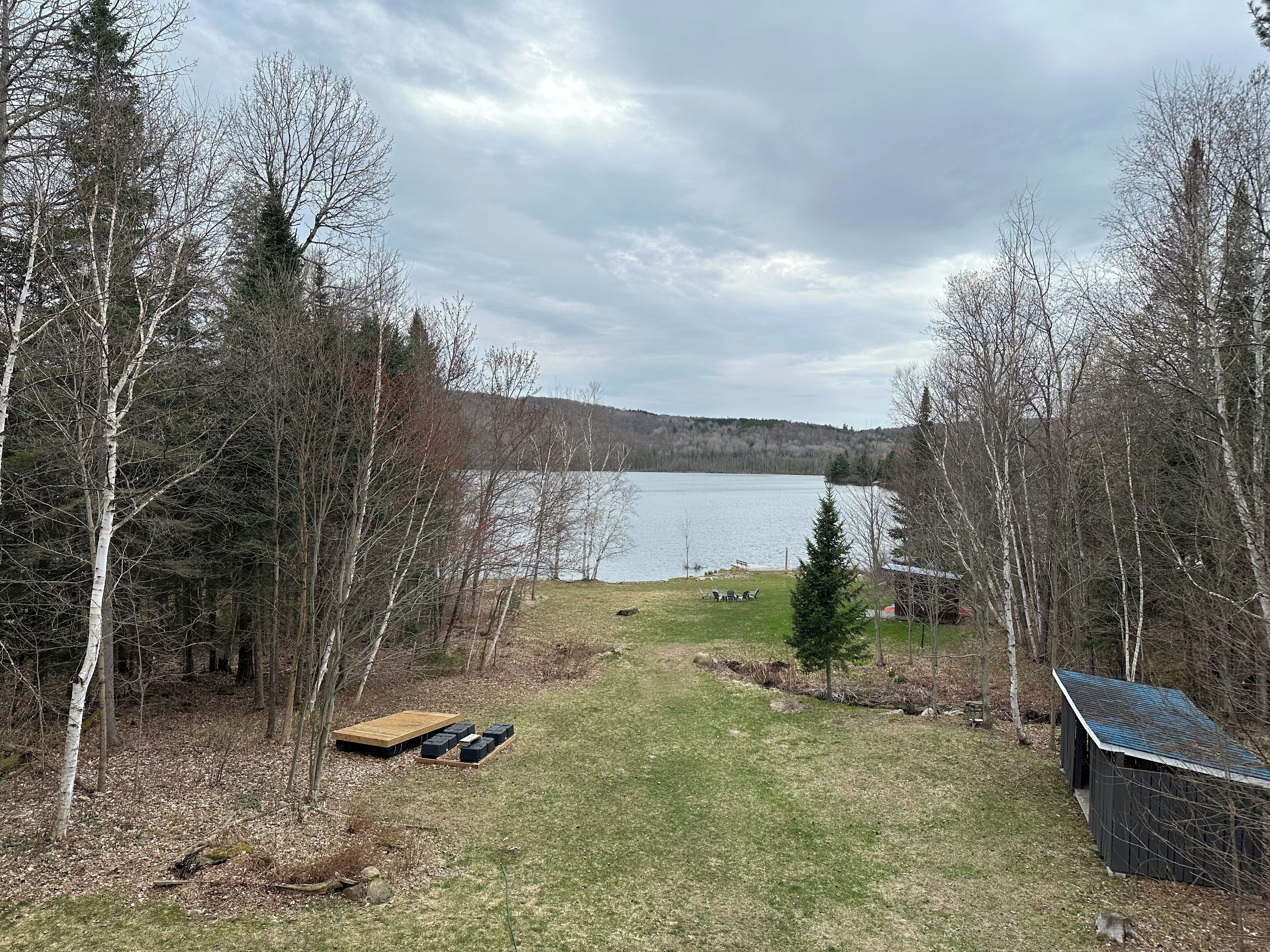 A lakeside property with a wooden deck, a small shed, and a grassy area.