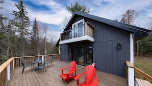 Een modern huis met een terras, twee rode Adirondack-stoelen en een tafel.