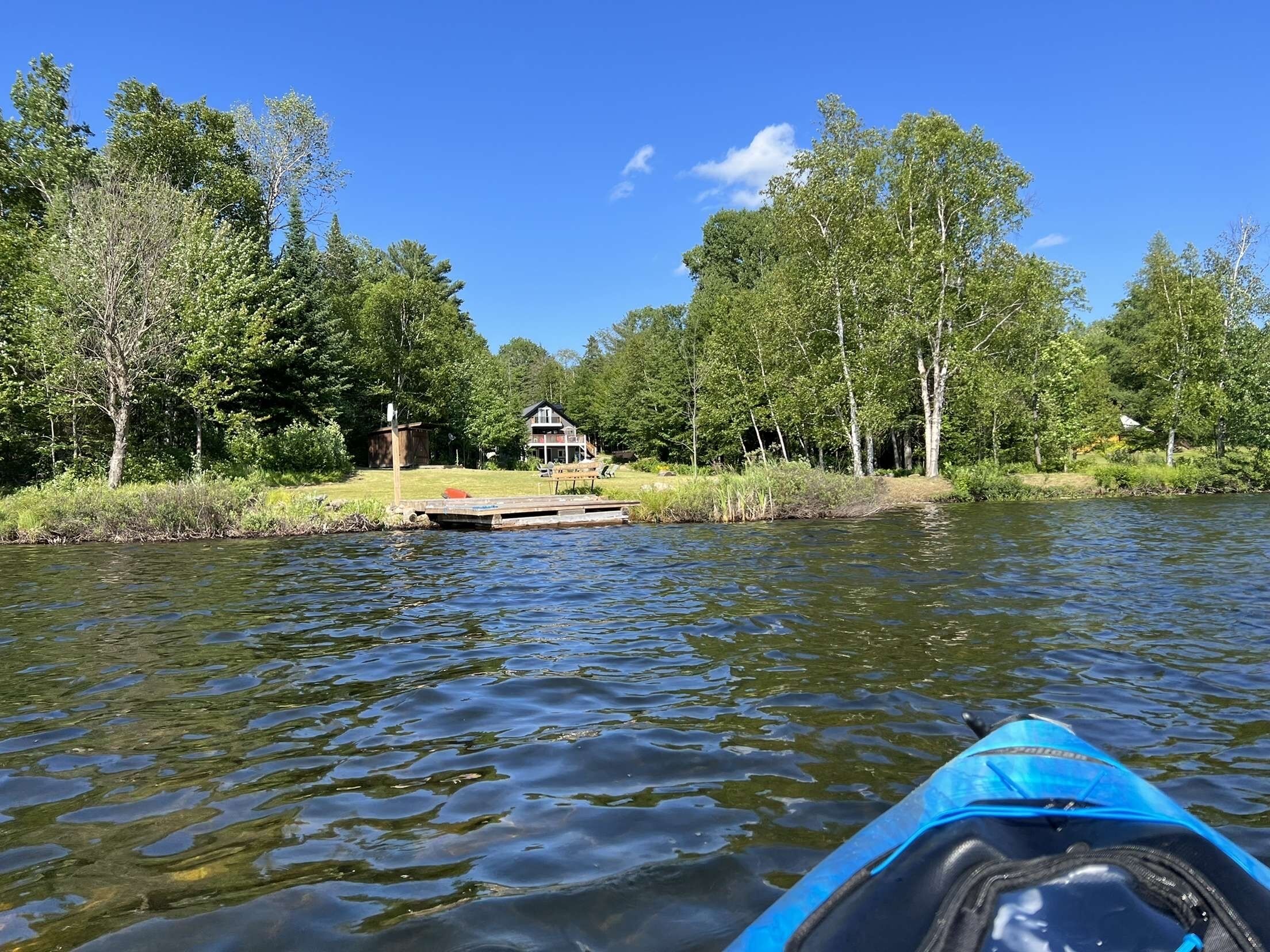 A calm lake with a dock and a house in the background surrounded by trees.