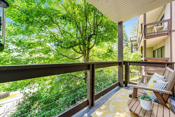 A balcony with a wooden railing, a potted plant, and a cushioned chair with a cushion.