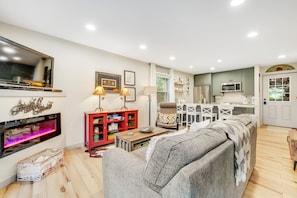 A modern living room with a fireplace, a red entertainment unit, a grey sofa, and a kitchen area with white cabinets and a microwave.