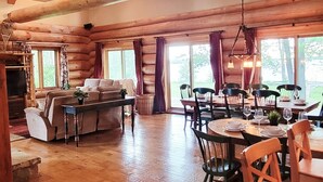 A spacious room with wooden beams, a large window, a sofa, and a dining table set for six. - Beautiful Chalet on the Lake! (Carleton Place)