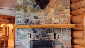A stone fireplace with a mounted buffalo head, a wooden mantel, and a log wall. - Beautiful Chalet on the Lake! (Carleton Place)