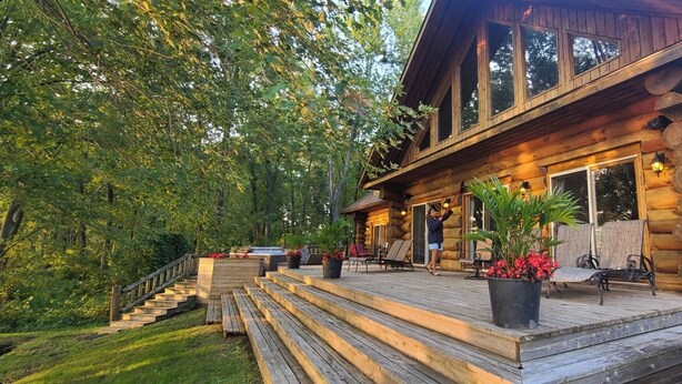 A log cabin with a wooden deck, outdoor seating, and a staircase leading to the entrance. - Beautiful Chalet on the Lake! (Carleton Place)