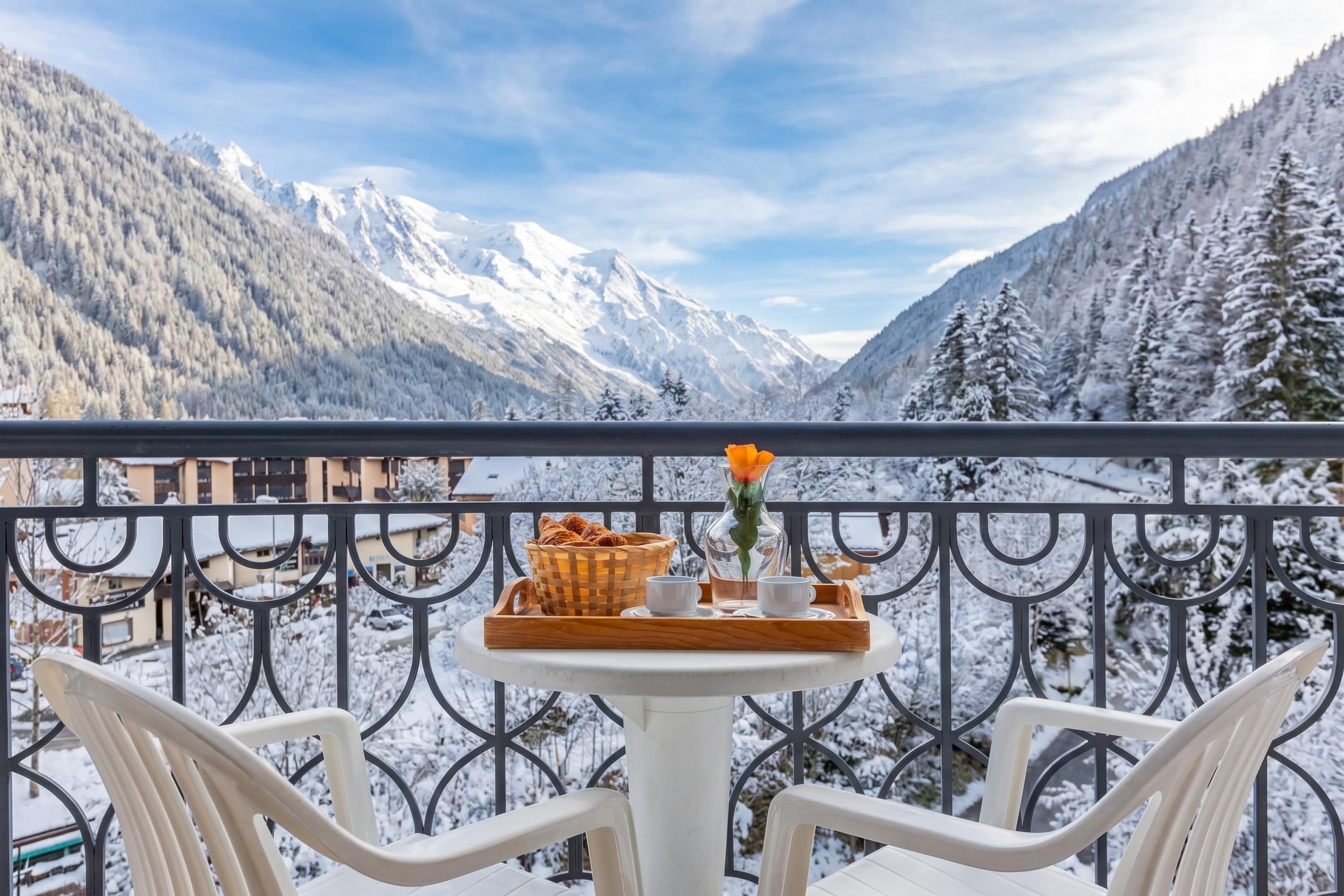 Un balcon avec une table dressée pour deux personnes, offrant une vue sur des montagnes enneigées.