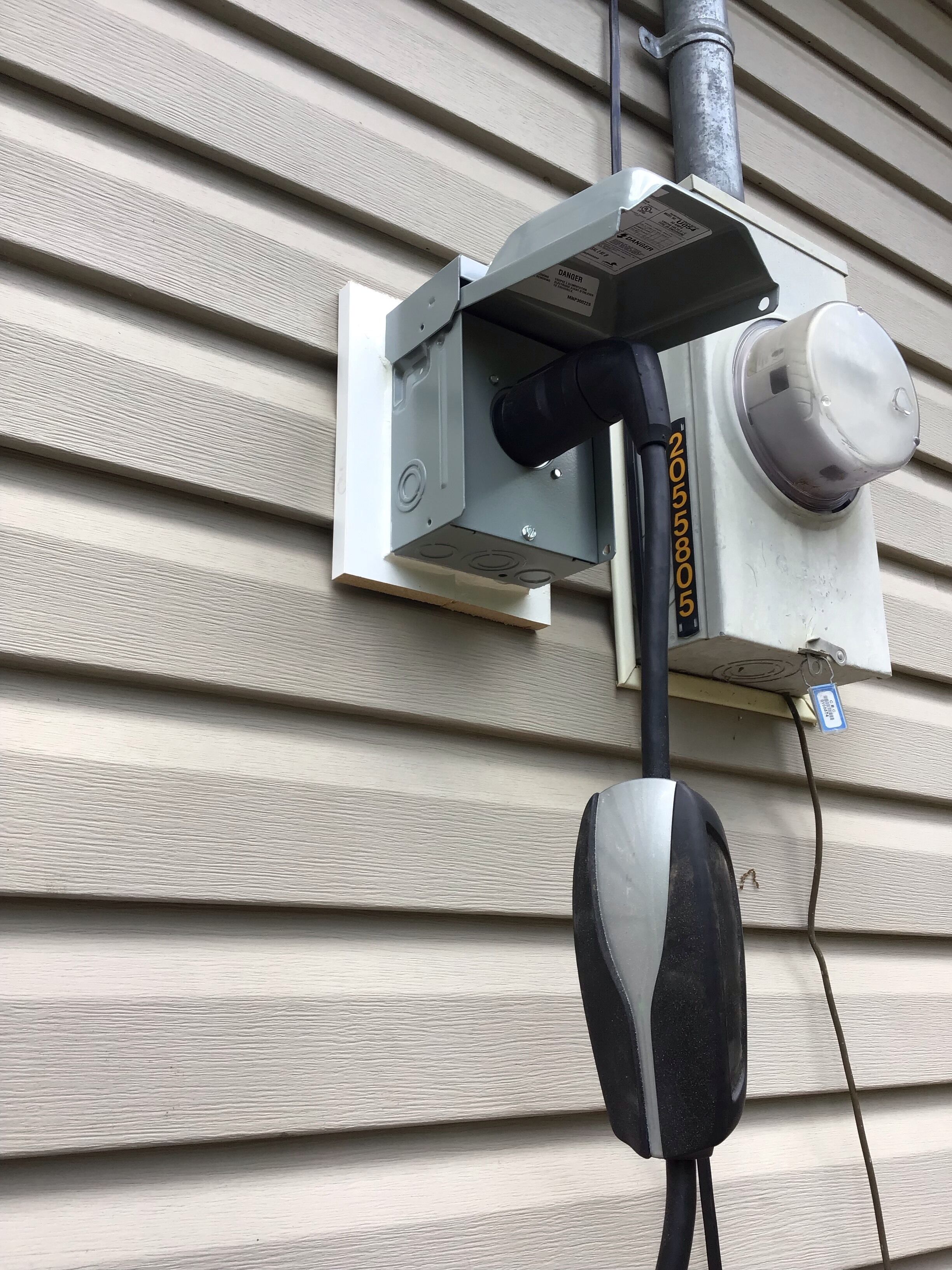A utility box mounted on a house with a metal bracket, a black cable, and a white cylindrical object.