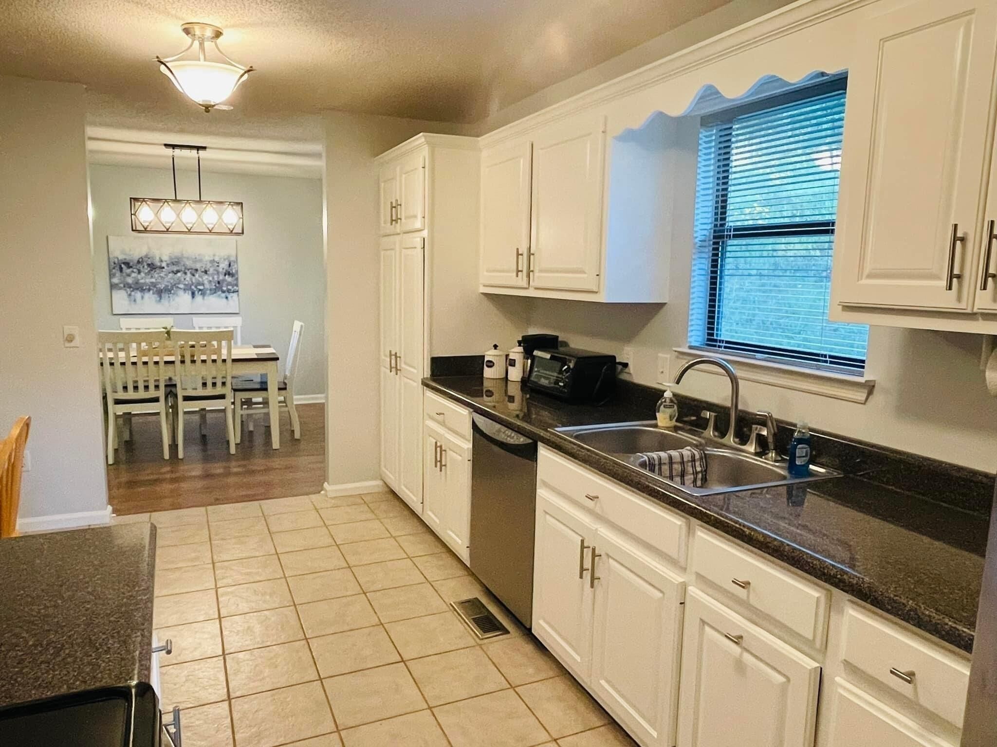 A kitchen with white cabinets, a black countertop, and a window with blinds.