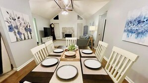 Un comedor con una mesa larga dispuesta para seis comensales, sillas blancas y una pieza decorativa central.
