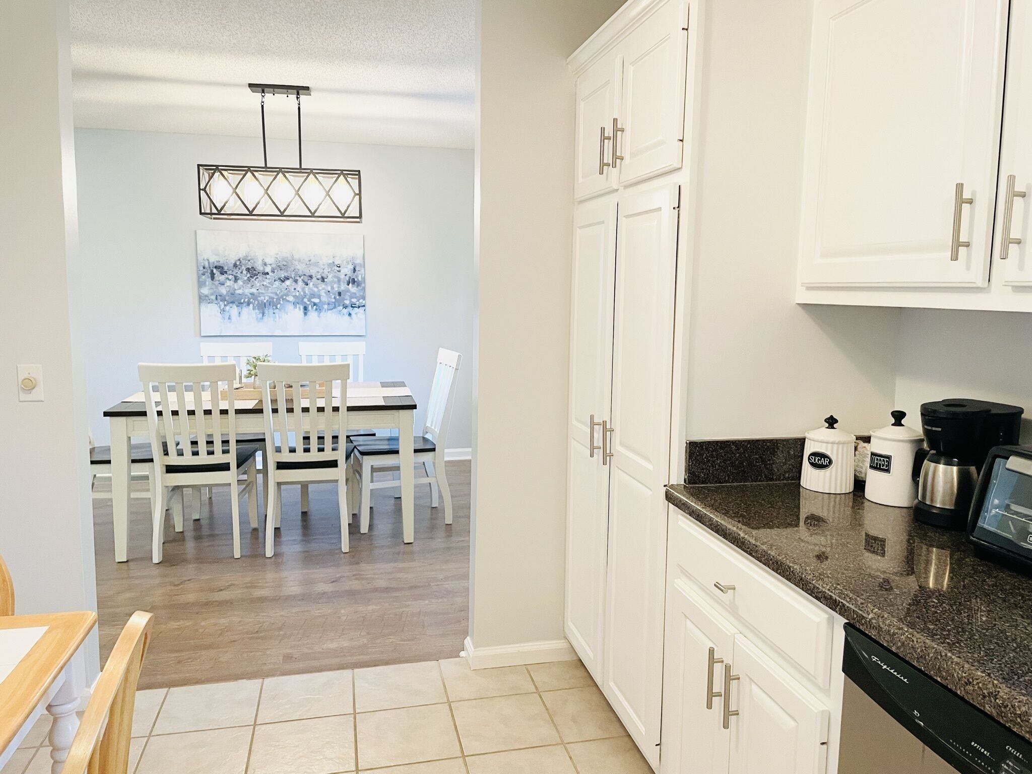 A kitchen with white cabinets, a granite countertop, and a dining area with a table and chairs.