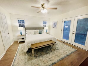 Cozy retreat with a large bed, nightstands, and a ceiling fan, set against a backdrop of a large window and a patterned rug.