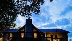 Una casa de dos pisos con una chimenea destacada, un balcón y un porche con luces.