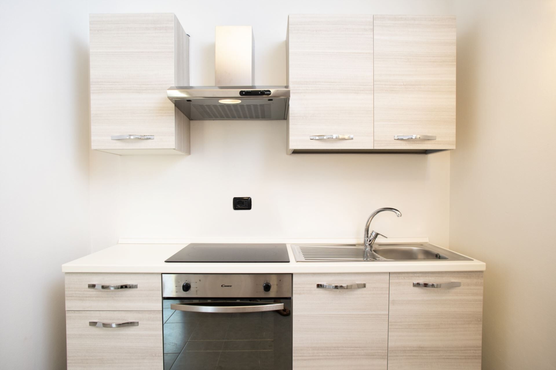 Una cocina moderna con armarios de madera clara, un lavamanos de acero inoxidable y un horno empotrado.