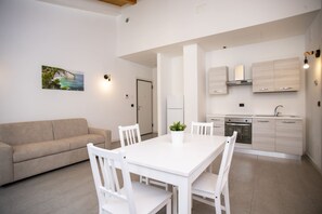Una cocina moderna con armarios blancos, horno empotrado y una zona de comedor con una mesa y sillas blancas.
