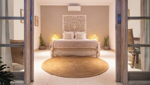 A modern bedroom with a large bed, two bedside lamps, a decorative wall piece, and a wicker chair in the background.