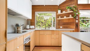 Eine moderne Küche mit Holzschränken, einer Edelstahl-Spüle und einem Fenster mit Blick auf Grünflächen.